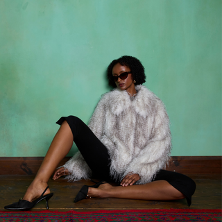 Woman in a fur coat sitting on a wooden bench against a green wall